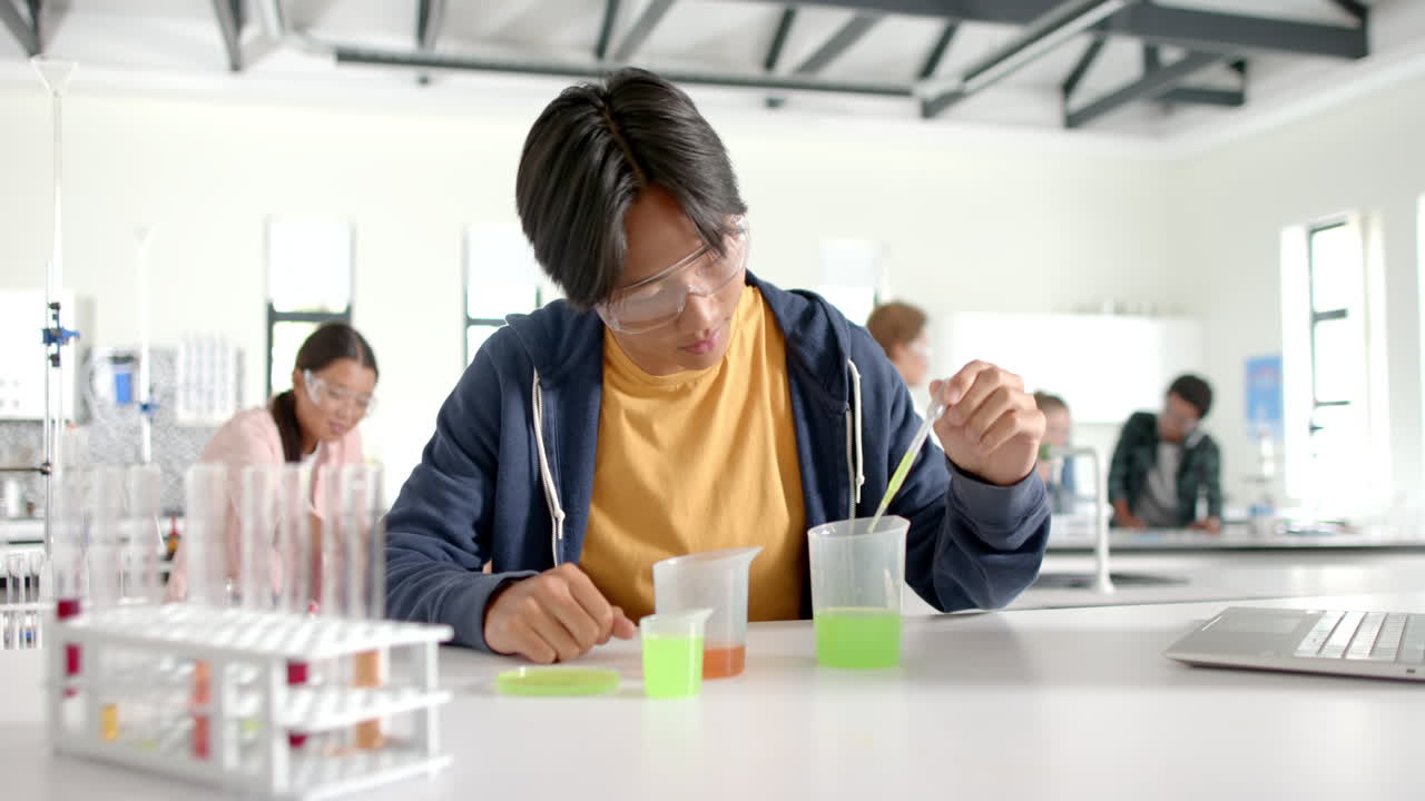 In high school laboratory, teenager conducting experiment with beakers and test tubes