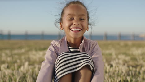 portrait of cute little mixed race girl sitting laughing cheerful enjoying sunny seaside park playful happy