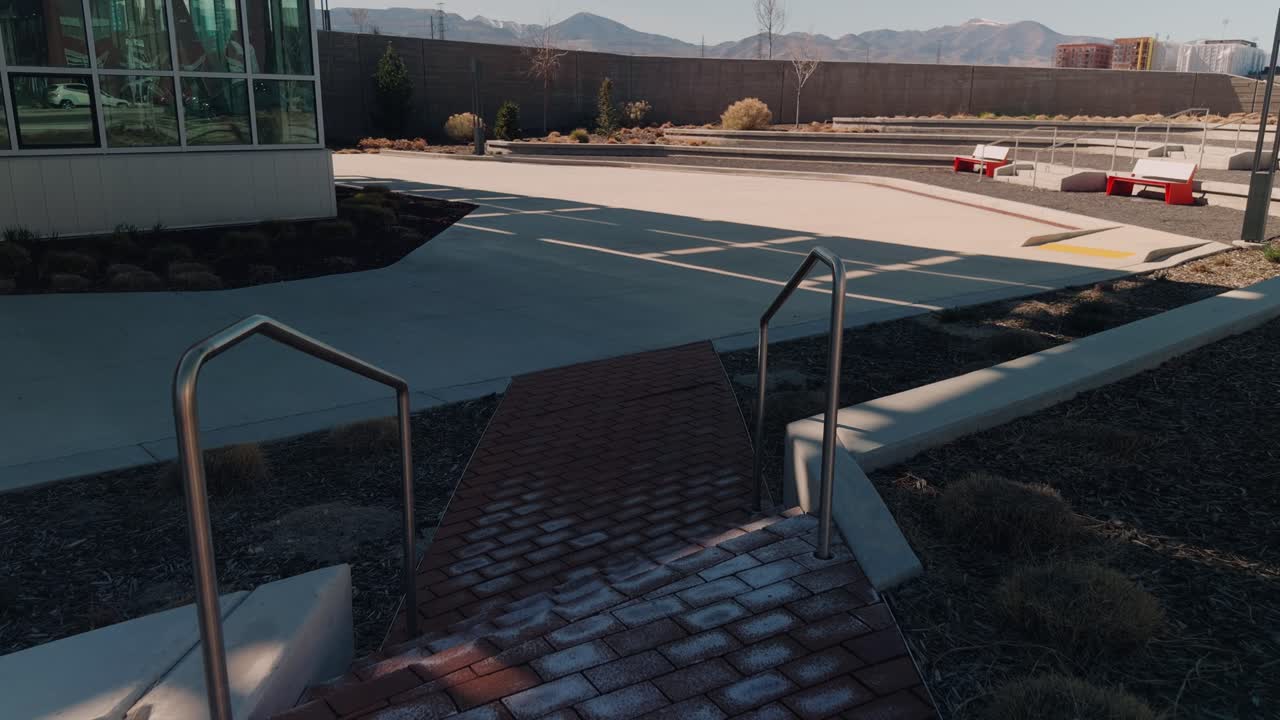 Dezentes Hineingleiten entlang eines Backsteinwegs zu einem modernen Platz mit Bergkulisse.