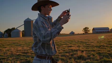 young farmer taking photo of sunset over farmland
