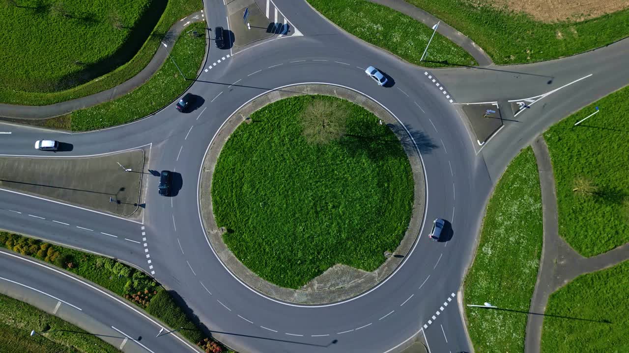 Cars driving on roundabout with green grass center, transportation, infrastructure and road network. Aerial drone top-down ascending