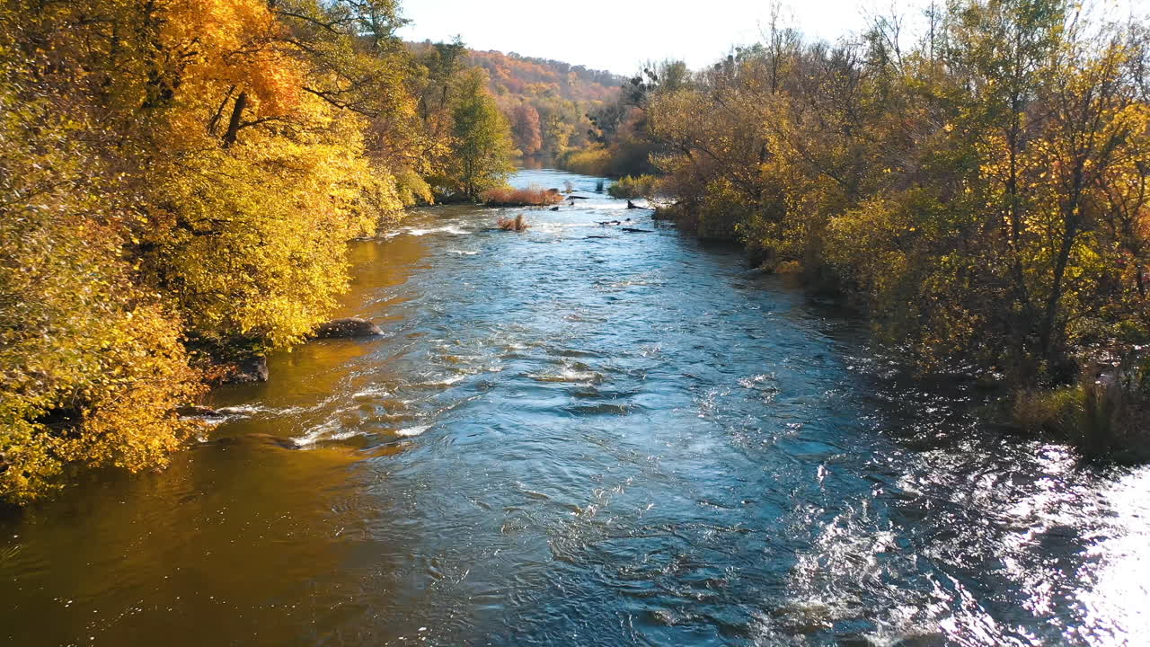 Beautiful river in autumn time at sunlight. Flight over blue water flowing among stones quickly in mountainous area. Amazing nature in fall.