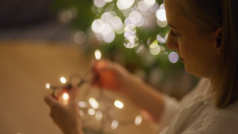 mujer en el interior acogedor de la casa organiza luces de navidad