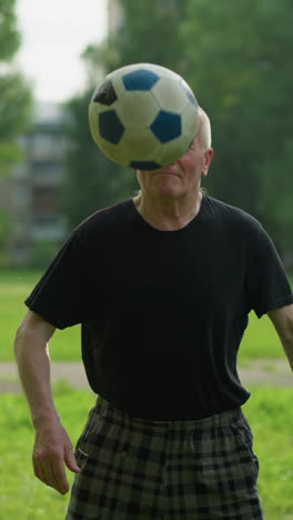 ein älterer mann spielt geschickt mit einem fußball auf einem üppigen grasbewachsenen feld und balanciert ihn mühelos auf seinem knie, mit bäumen und einem entfernten torpfosten im hintergrund