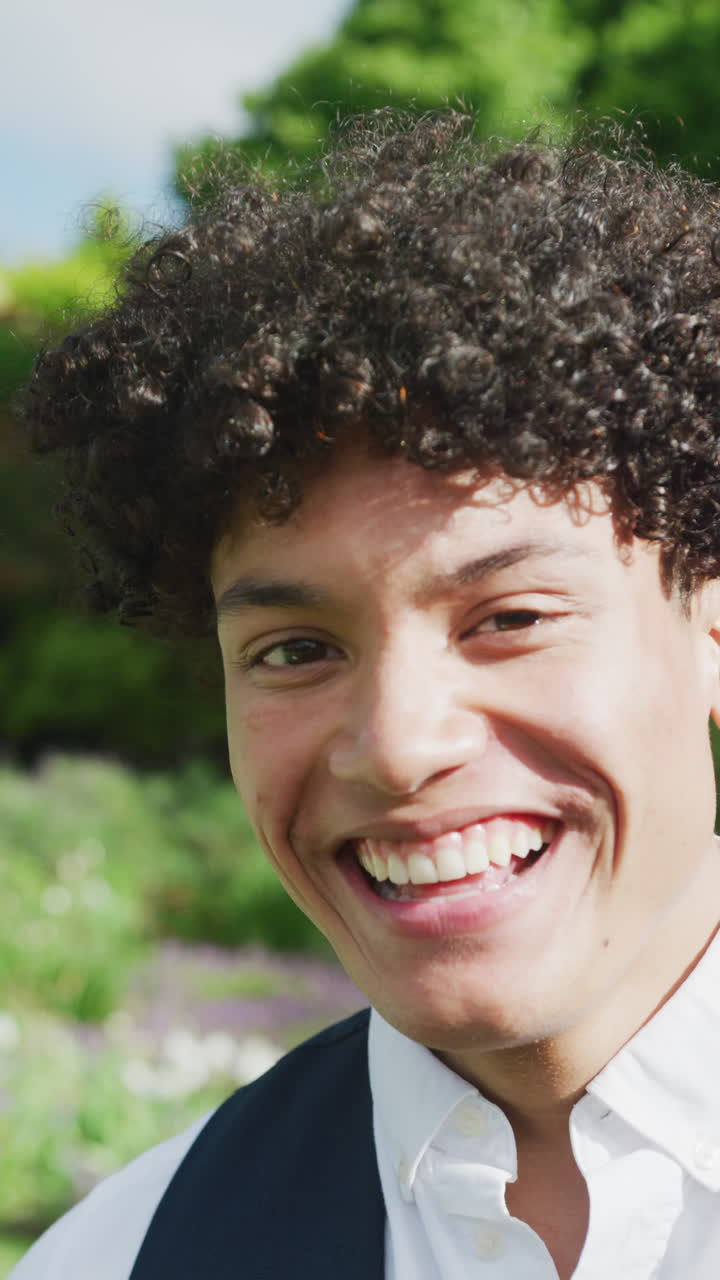 video vertical del retrato de un hombre biracial feliz en el jardín en un día soleado en una boda