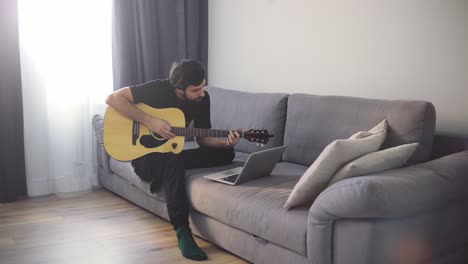 A-young-man-plays-the-guitar-through-a-video-call-on-a-laptop