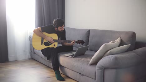 a young man plays the guitar through a video call on a laptop