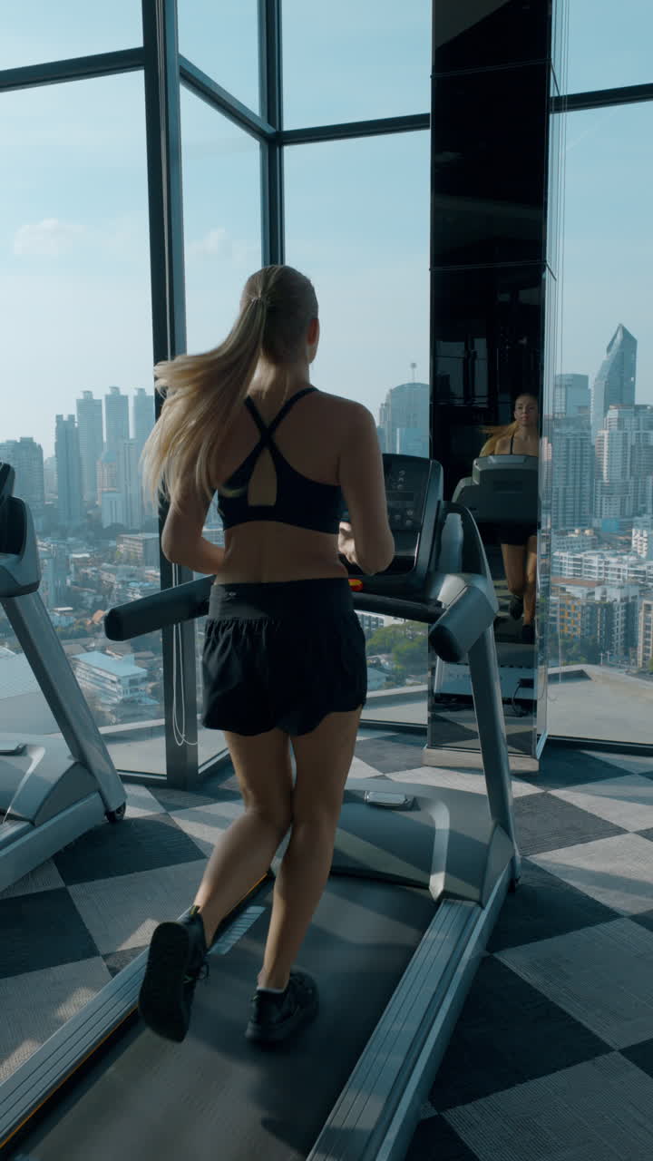 Woman running on a treadmill in a high-rise gym with a city view ...