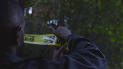 black officer strings up caution tape in a wooded area