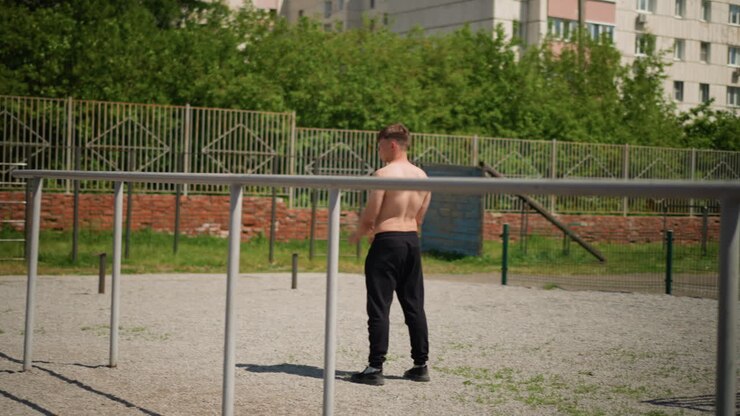 male engages in outdoor workout, individual exercises casually among trees and fences during daytime, man participates in informal physical activity outdoors in vibrant city park setting