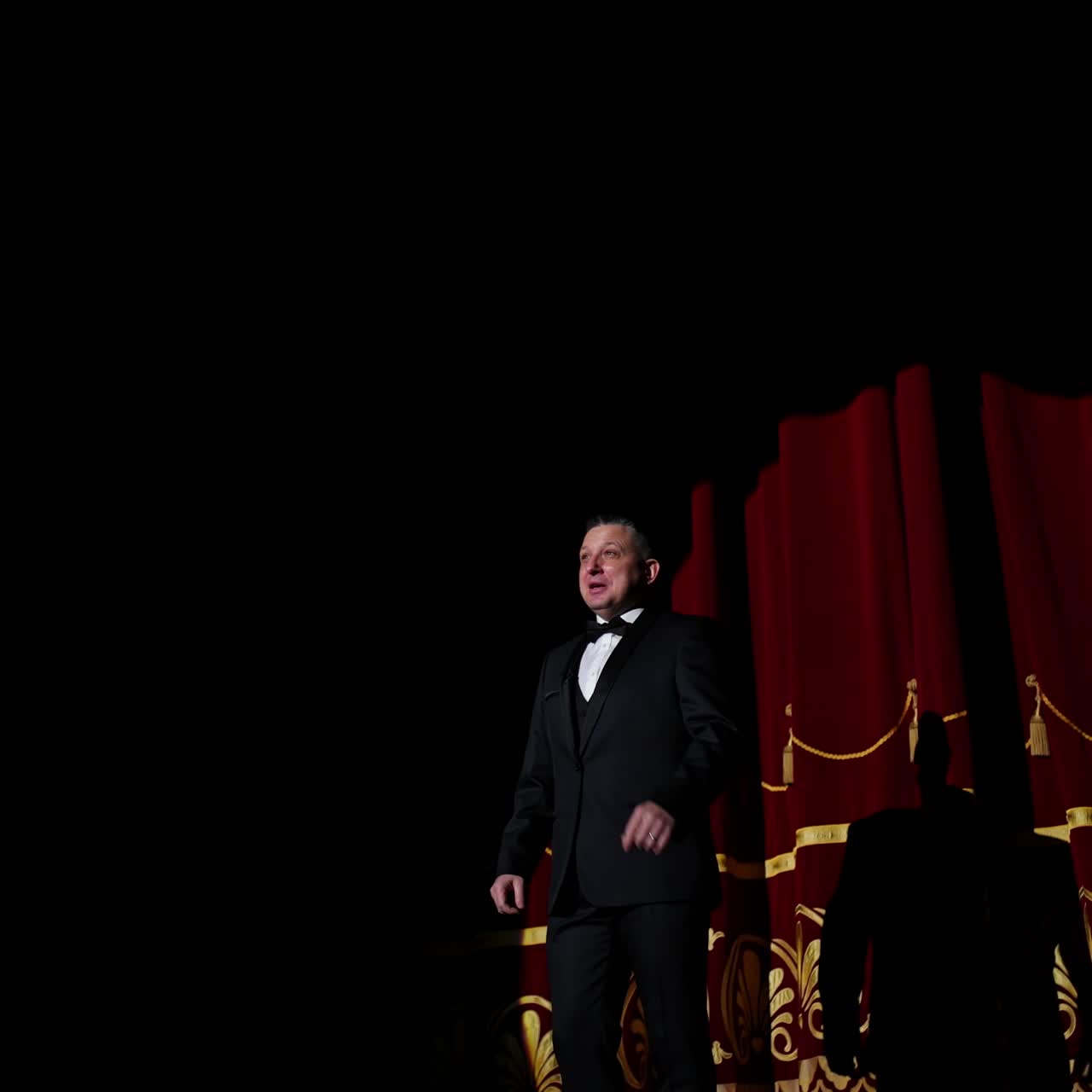 Male performer on stage. Actor in elegant suit presenting the performance in the theater. Comedian appears on the scene. Light spot on dark background