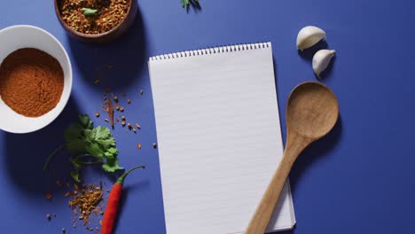 video of notepad with copy space, spoon and seasoning lying on violet background