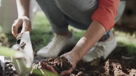 low section of senior caucasian woman preparing soil with hands and trowel in garden, slow motion