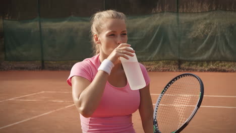 woman drinking water on a tennis court