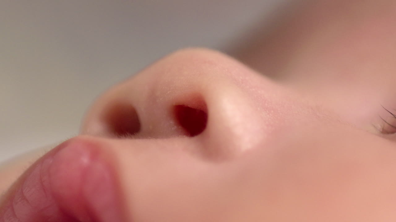 Close-up shot of the nostrils of a sleeping newborn child and showing her upper lip and some parts of her lashes