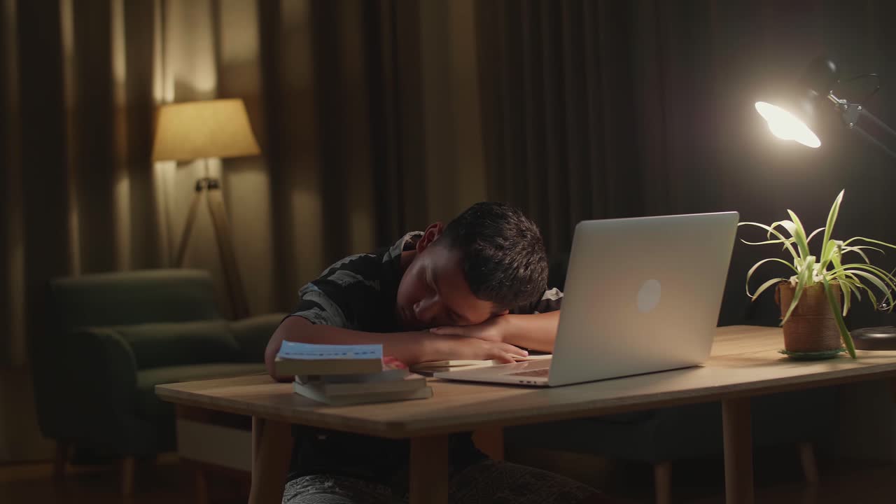 Tired Teenage Boy Sleeping On The Table At Home After Doing Home Work At Night Time