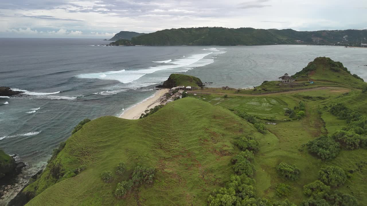 Flyover lush coastal hill reveals secluded sand surf beach on Lombok