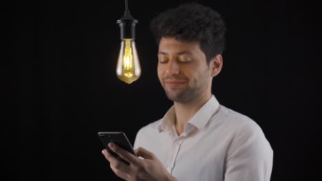 Der-Mann,-Der-Auf-Das-Telefon-Schaut,-Hat-Eine-Neue-Idee-Und-Die-Lampe-Geht-An.-Heureka