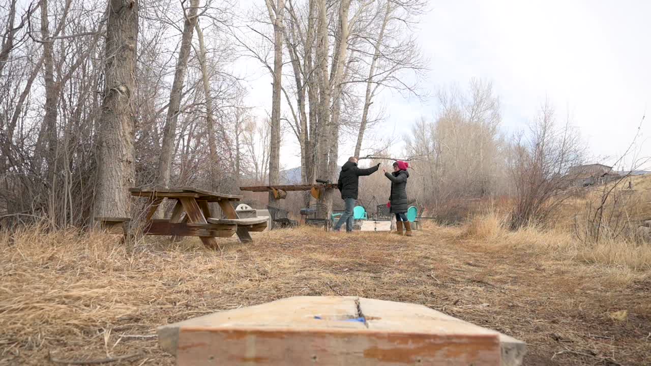 Male throwing a cornhole bag into a cornhole and celebrating with female partner, static
