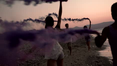 multi-ethnic friends celebrating with smoke bombs at beach at sunset
