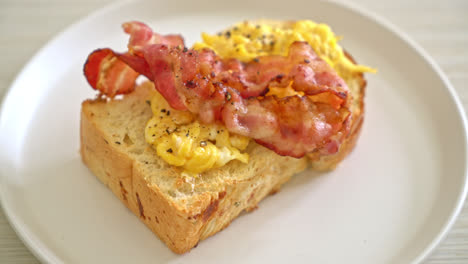 pan tostado con huevos revueltos y tocino en un plato blanco