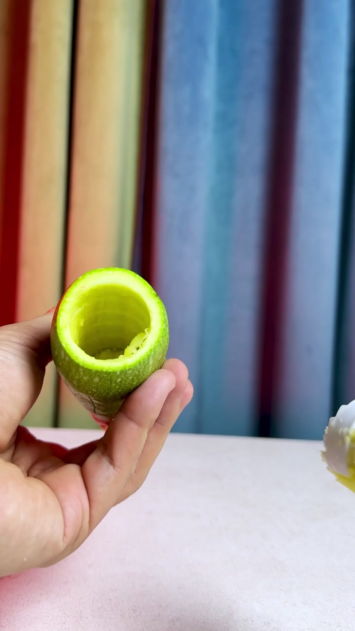 Un gros plan vertical de mains utilisant un ustensile de cuisine en plastique pour évider une courgette verte fraîche. Cette préparation culinaire saine a lieu à l'intérieur sur une table, sur un fond flou et coloré