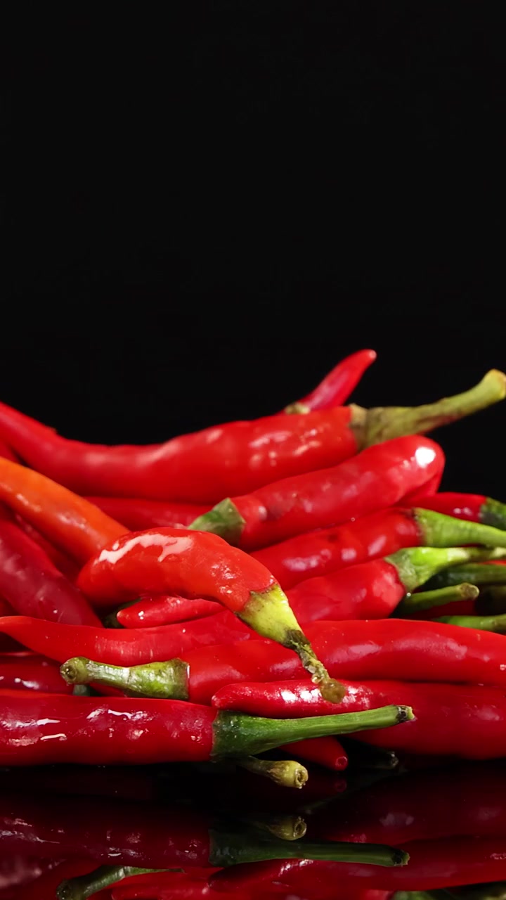 A vibrant pile of red chili peppers rotates smoothly on a glossy black surface with dramatic studio lighting and a seamless, reflective background