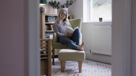 woman reading a book in a comfortable chair at home