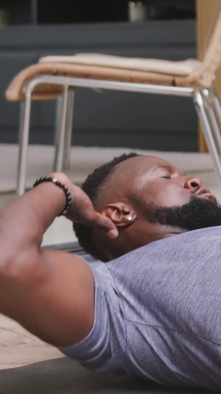 Video verticale: Uomo che inspira, in maglietta grigia e pantaloni neri, che solleva il busto e ruota sul tappetino per il core