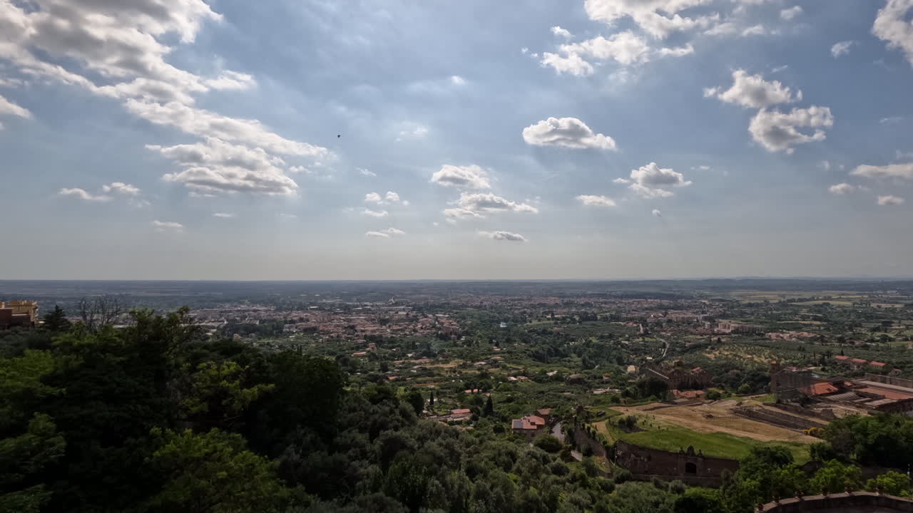 Splendida vista panoramica di Tivoli, Italia, che si affaccia sulla vasta campagna romana con alberi verdi e rigogliosi, tetti in terracotta e un cielo drammatico pieno di nuvole che si estende verso Roma.