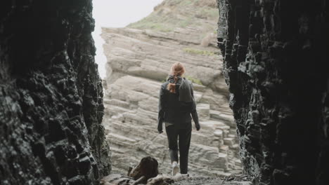 person exiting a dark cave into a rocky landscape