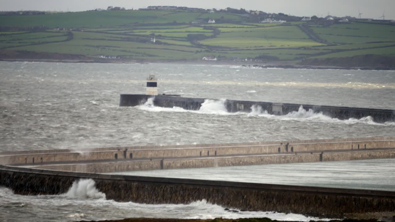 Huge bad weather waves crashing over Holyhead breakwater pier and Welsh lighthouse landmark