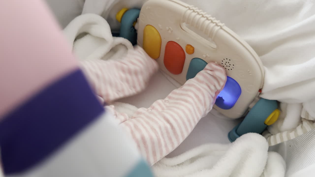 Close up - baby kicking colorful musical toy while lying on soft blanket