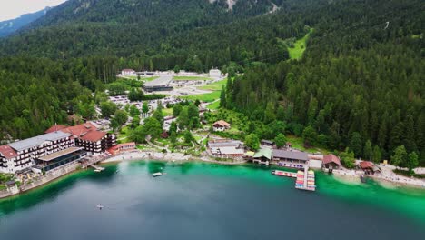 Luftaufnahme-Des-Wunderschönen-Smaragdgrünen-Wassers-Des-Eibsees-In-Bayern,-Deutschland,-Mit-Einem-Seebad-Am-Fuße-Der-Zugspitze,-Umgeben-Von-Einem-Pinienwald