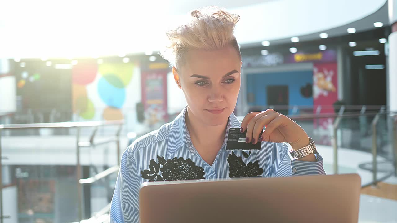 Woman using laptop and credit card in a shopping mall