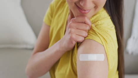 mujer asiática feliz sentada en el sofá mostrando el brazo con yeso después de la vacunación