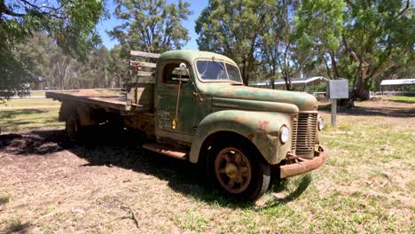 old green truck stationary in a sunny, tree-filled area