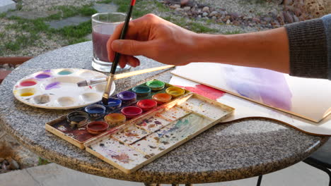 an artist dipping his brush in blue water color paint making an abstract artwork in an outdoor studio