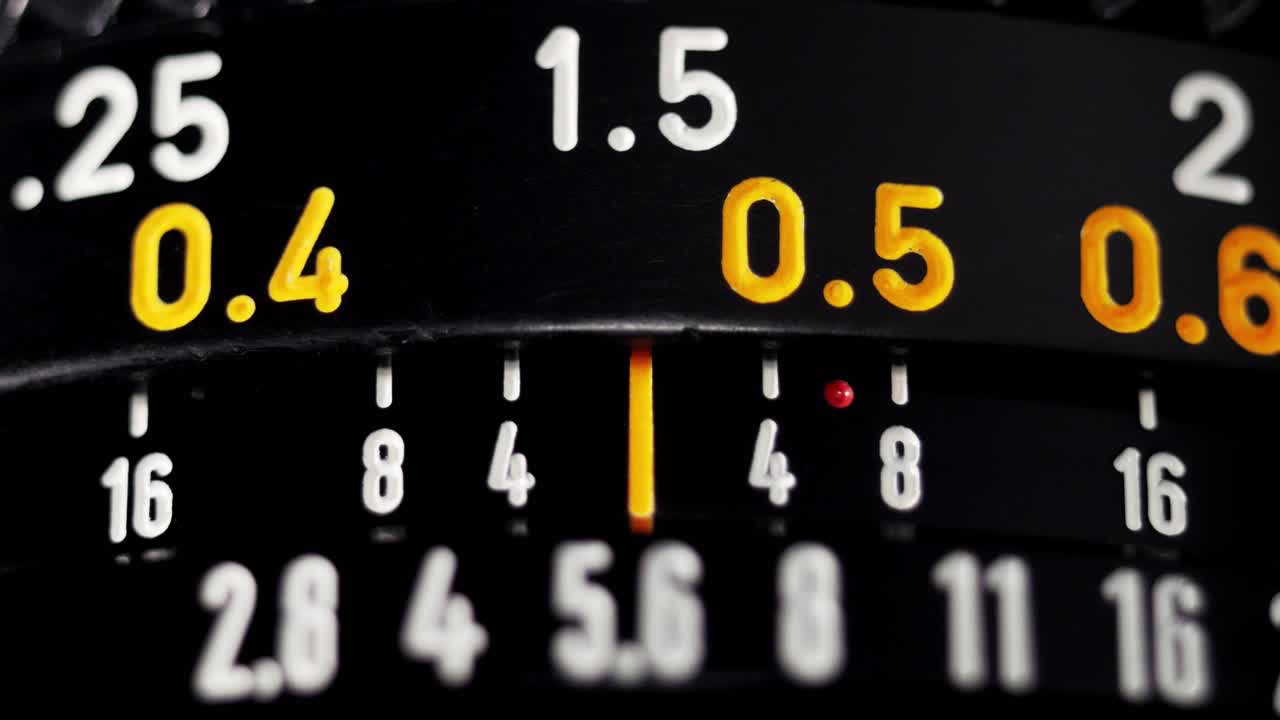 Macro focus pull on black vintage camera lens with orange distance scale numbers