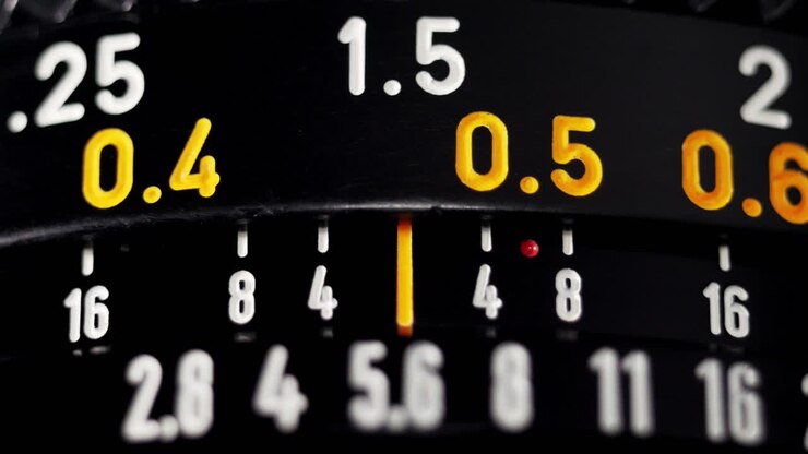 Macro focus pull on black vintage camera lens with orange distance scale numbers