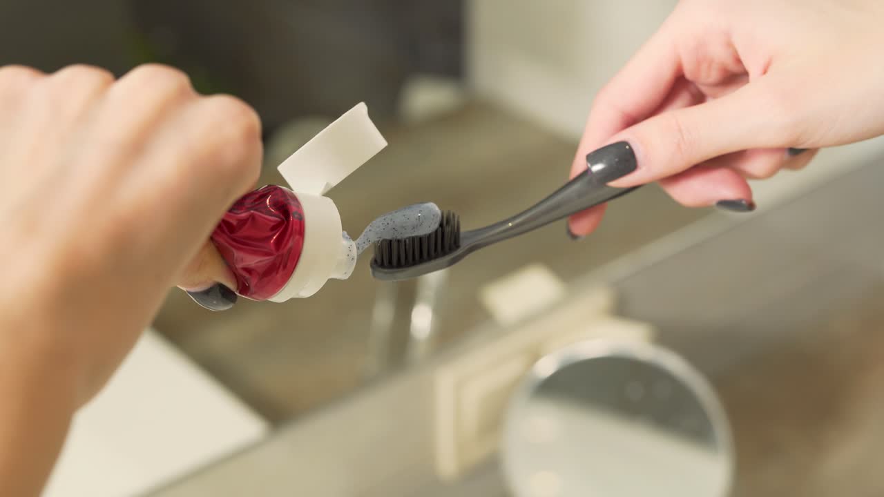 Close-up scene of a woman who is putting some amount of toothpaste on a toothbrush