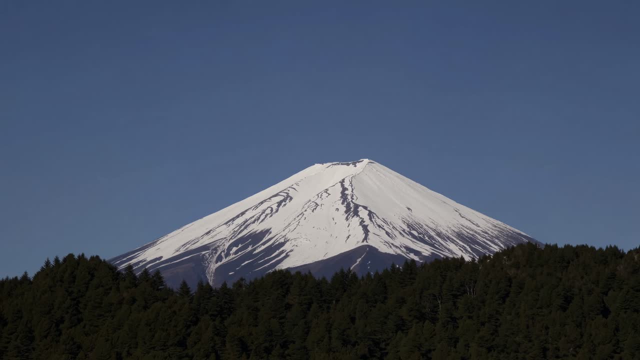 A stunning video still of a snow-capped mountain peak, captured from a low angle against a clear