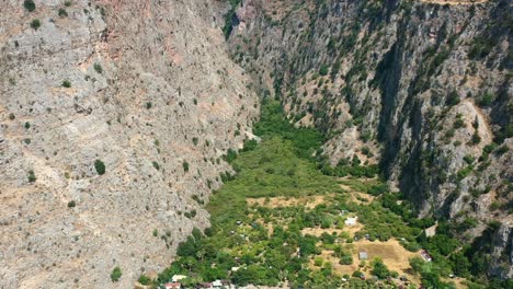 aerial-drone-panning-down-at-butterfly-valley-in-Fethiye-Turkey-overlooking-tourist-boats-docked-on-a-white-sand-beach-on-a-sunny-summer-day-surrounded-by-large-rocky-mountains