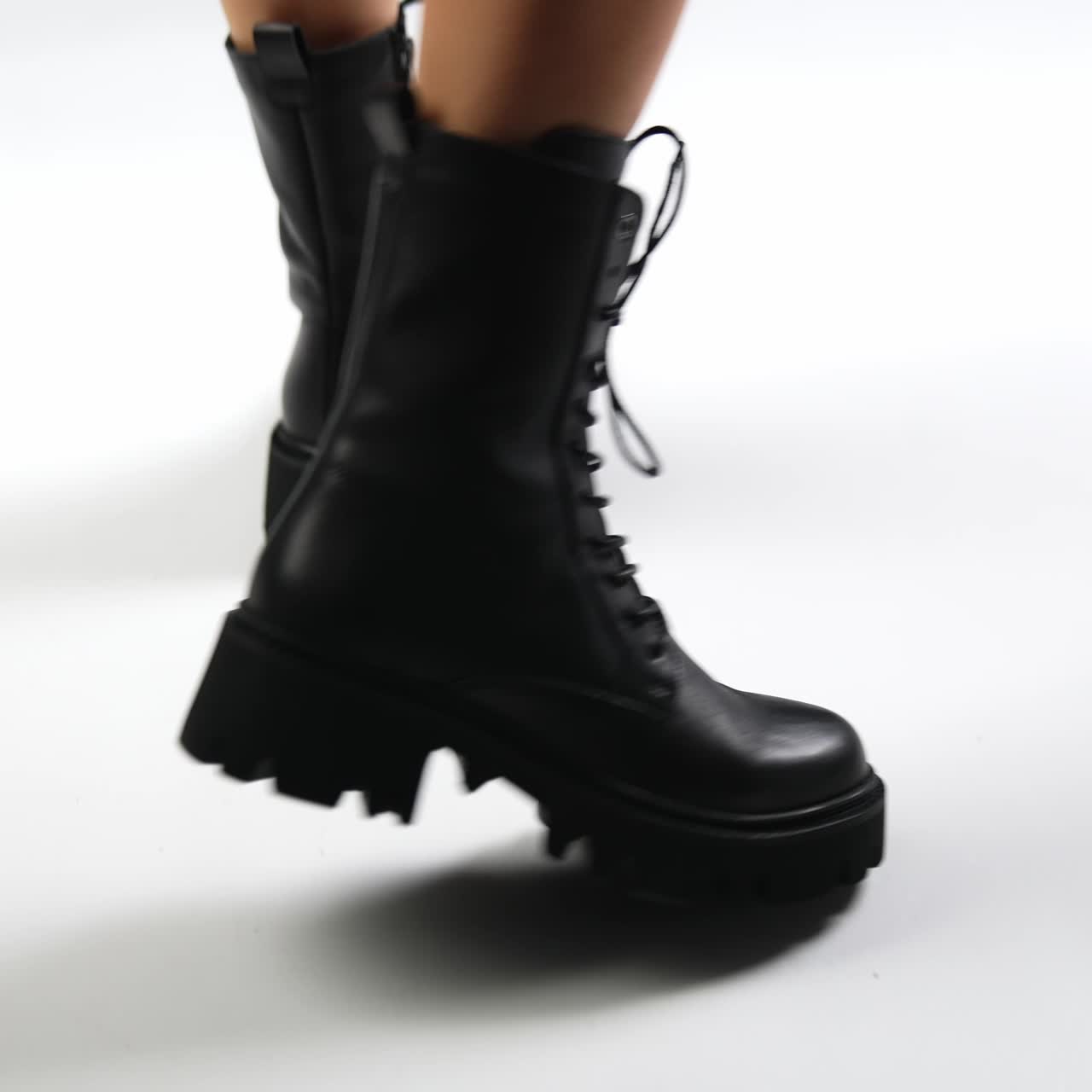 Female model walks in black leather boots with tractor soles and laces. Fashionable elegant footwear demonstration