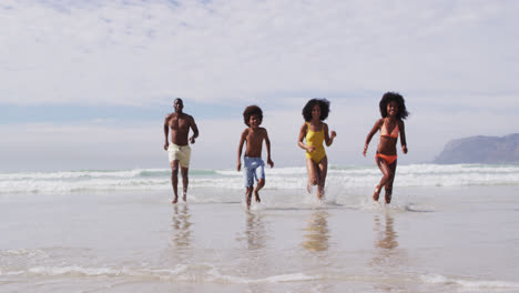 african american parents and two children running at the beach