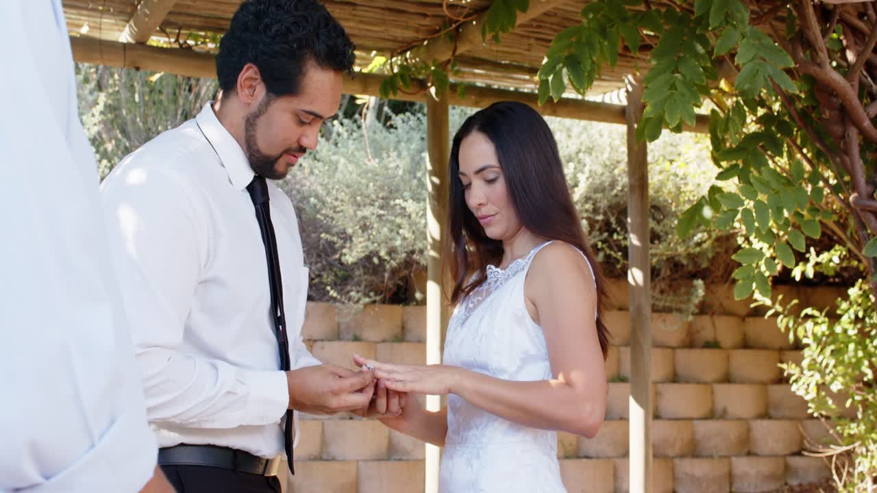 Vertical video: Opening blue box groom placing ring on bride's left finger in garden wedding dress