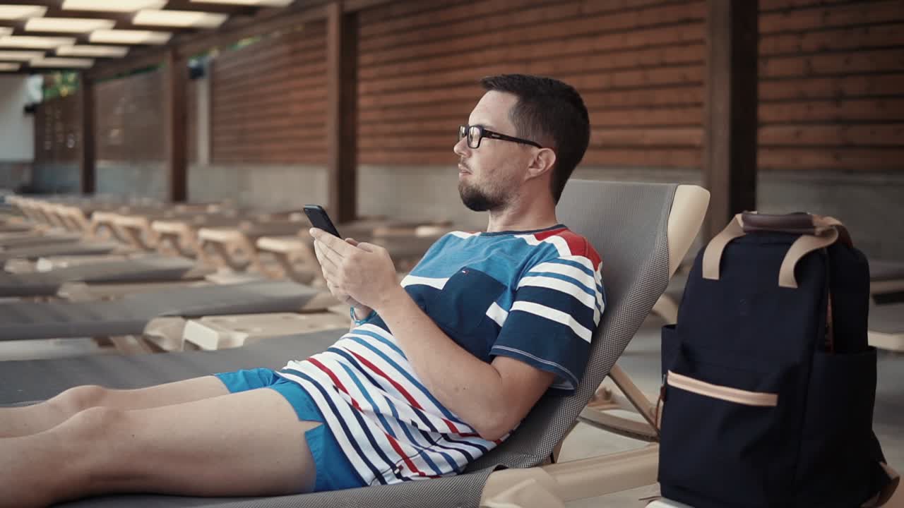 hombre relajándose junto a la piscina con un teléfono inteligente