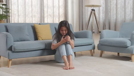 a woman sitting on the floor, crying and looking at her phone.