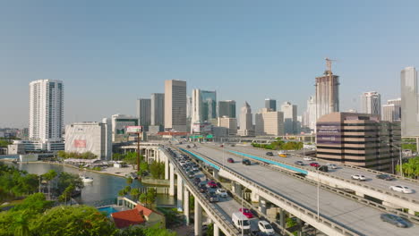 Aerial-shot-of-traffic-jam-on-exit-ramp.-Cars-driving-on-elevated-wide-highway-in-city.-Modern-city-borough-in-background.-Miami,-USA