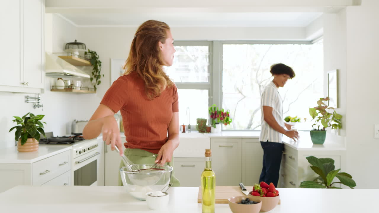 Diverse couple enjoying cooking together in bright kitchen, preparing fresh ingredients, at home
